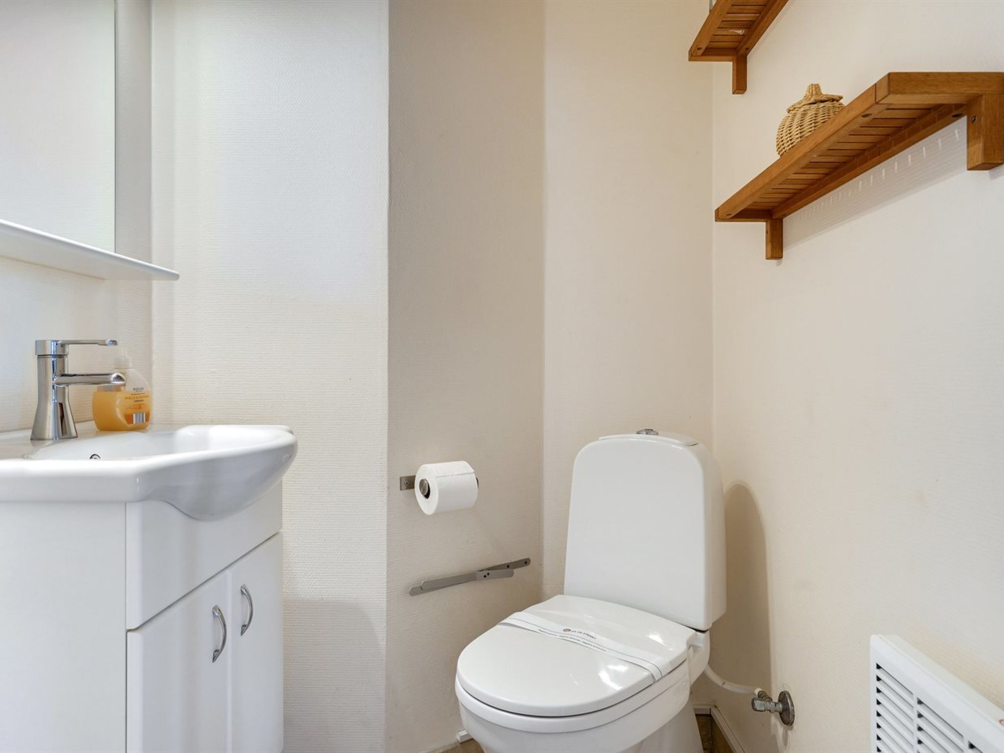 Une salle de bain avec un lavabo blanc, des toilettes et une étagère en bois au-dessus des toilettes.