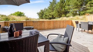An outdoor deck with wicker furniture, a table with a kettle and cups, and a large umbrella.