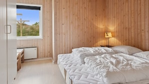 A bedroom with a wooden ceiling, a bed with white bedding, a bedside table, and a lamp.