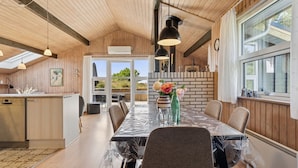 A modern kitchen with wooden cabinets, a dining area with a table set for four, and a large window providing a view of the outdoors.