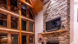 A spacious living room with a stone fireplace, leather furniture, and large windows. - Upscale 4BR mountain retreat with private hot tub, AC, and Mountain Club access. (Kimberley)