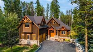 A large, multi-story log cabin with a stone foundation, multiple garage doors, and a driveway leading to the entrance. - Upscale 4BR mountain retreat with private hot tub, AC, and Mountain Club access. (Kimberley)