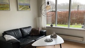 A modern living room with a black leather sofa, a white coffee table, and a large window with a view of a garden. - "Luise" - 800m from the sea by Interhome (Egernsund)