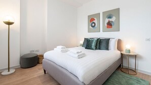 A modern bedroom with a large bed, two wall art pieces, a bedside lamp, and a floor lamp. - Leicester Square  flats by Joivy (London)