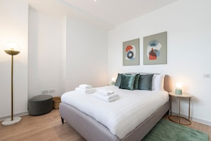 A modern bedroom with a large bed, two wall art pieces, a bedside lamp, and a floor lamp. - Leicester Square flats by Joivy (London)
