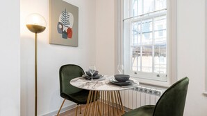 A dining area with a round table, two chairs, a floor lamp, and a window with a view. - Leicester Square  flats by Joivy (London)