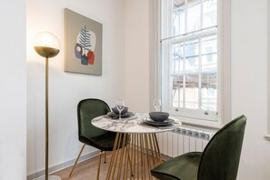 A dining area with a round table, two chairs, a floor lamp, and a window with a view. - Leicester Square flats by Joivy (London)