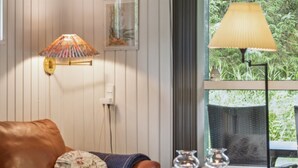 A cozy living room with a leather sofa, a table with decorative items, a wall-mounted lamp, and a window with a view of greenery. - "Alkmar" -  from the sea by Interhome (Hadsund)