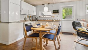 A kitchen with white cabinets, a dining table with blue chairs, and a wooden ceiling. - "Alkmar" -  from the sea by Interhome (Hadsund)