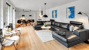 Ein modernes Wohnzimmer mit einer schwarzen Ledersofa, einem Essbereich mit schwarzen Stühlen und einer Küche im Hintergrund.