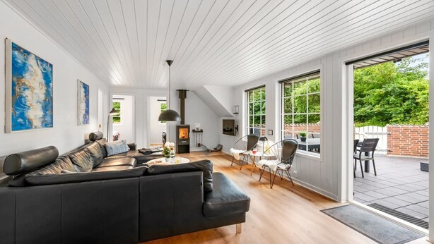 Ein geräumiges Wohnzimmer mit einem schwarzen Ecksofa, einem Kamin und großen Fenstern, die einen Blick ins Freie ermöglichen.