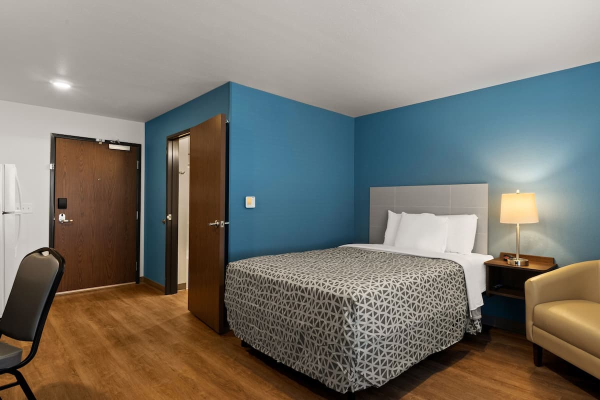 A hotel room with a bed, a chair, a nightstand, and a door.