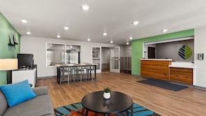 A modern office space with a reception desk, a dining area, and a seating area with a couch and a coffee table. - WoodSpring Suites Greeley (Greeley)