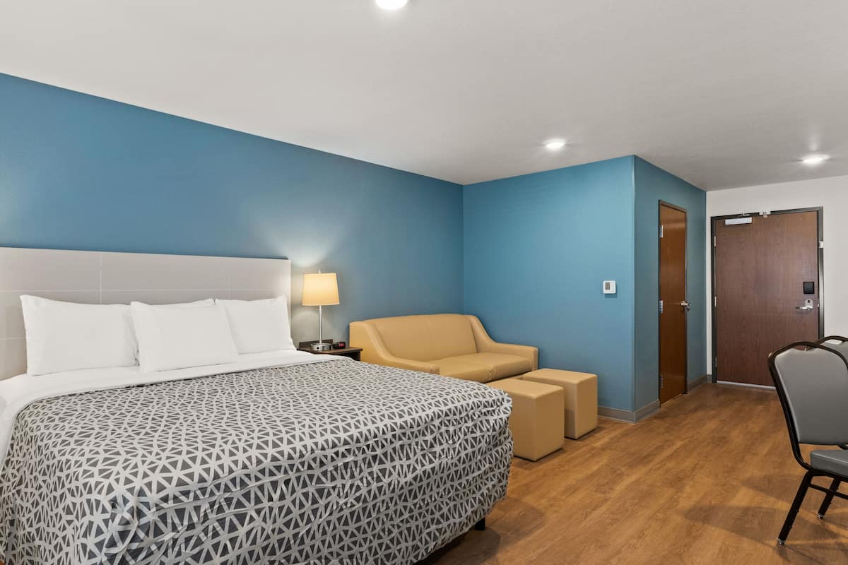 A hotel room with a bed, two bedside tables with lamps, a sofa, a chair, and a wooden door.