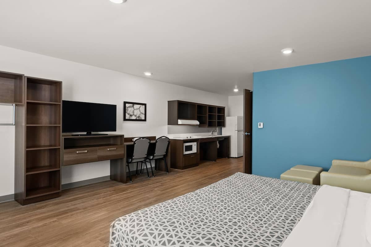 A modern bedroom with a bed, a desk, and a kitchenette.