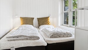 Ein Schlafzimmer mit zwei Betten, weißen Wänden und einem Fenster mit Blick auf Grünflächen.