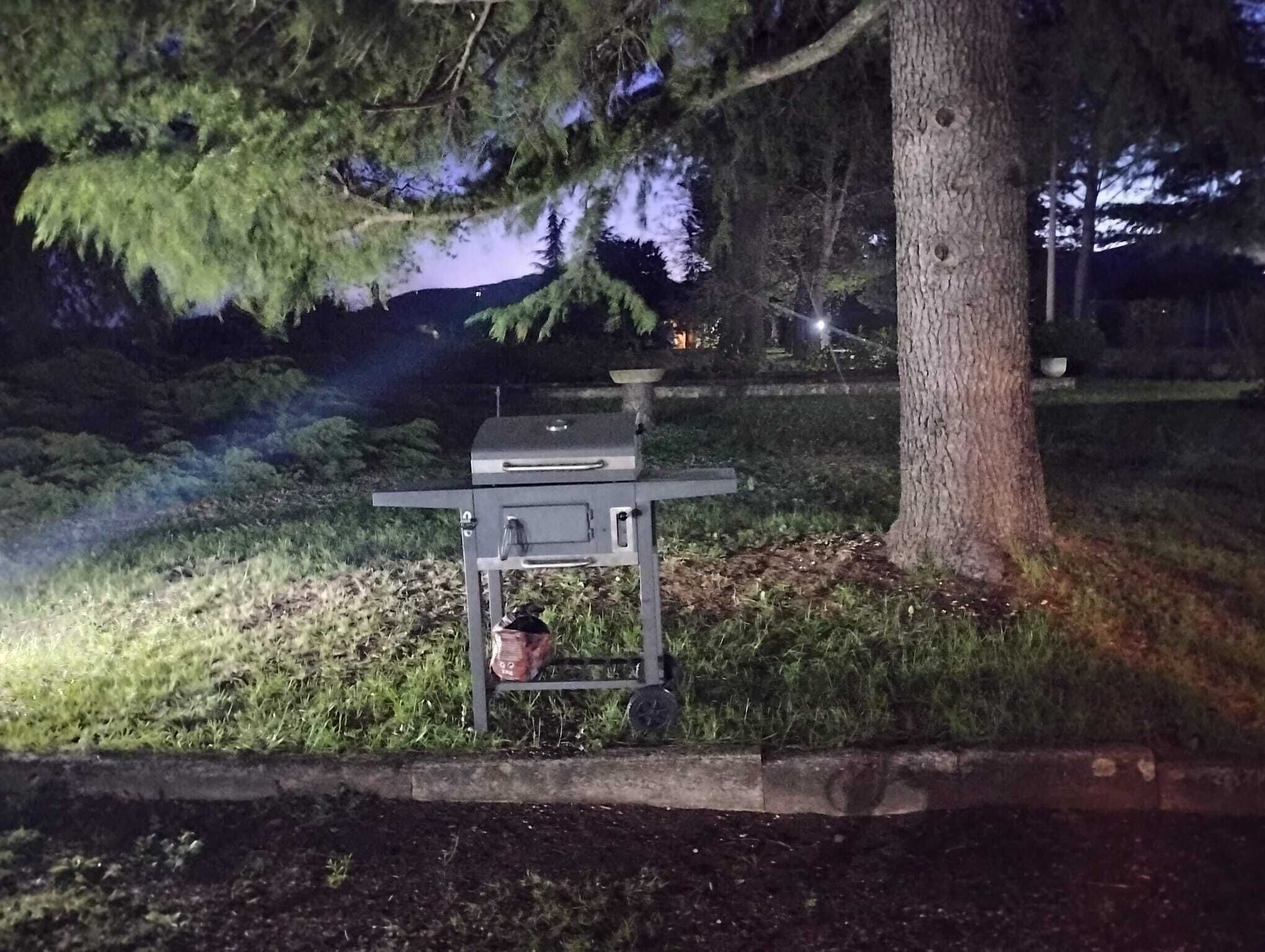 An outdoor grill setup with a table and a pot, surrounded by grass and trees.