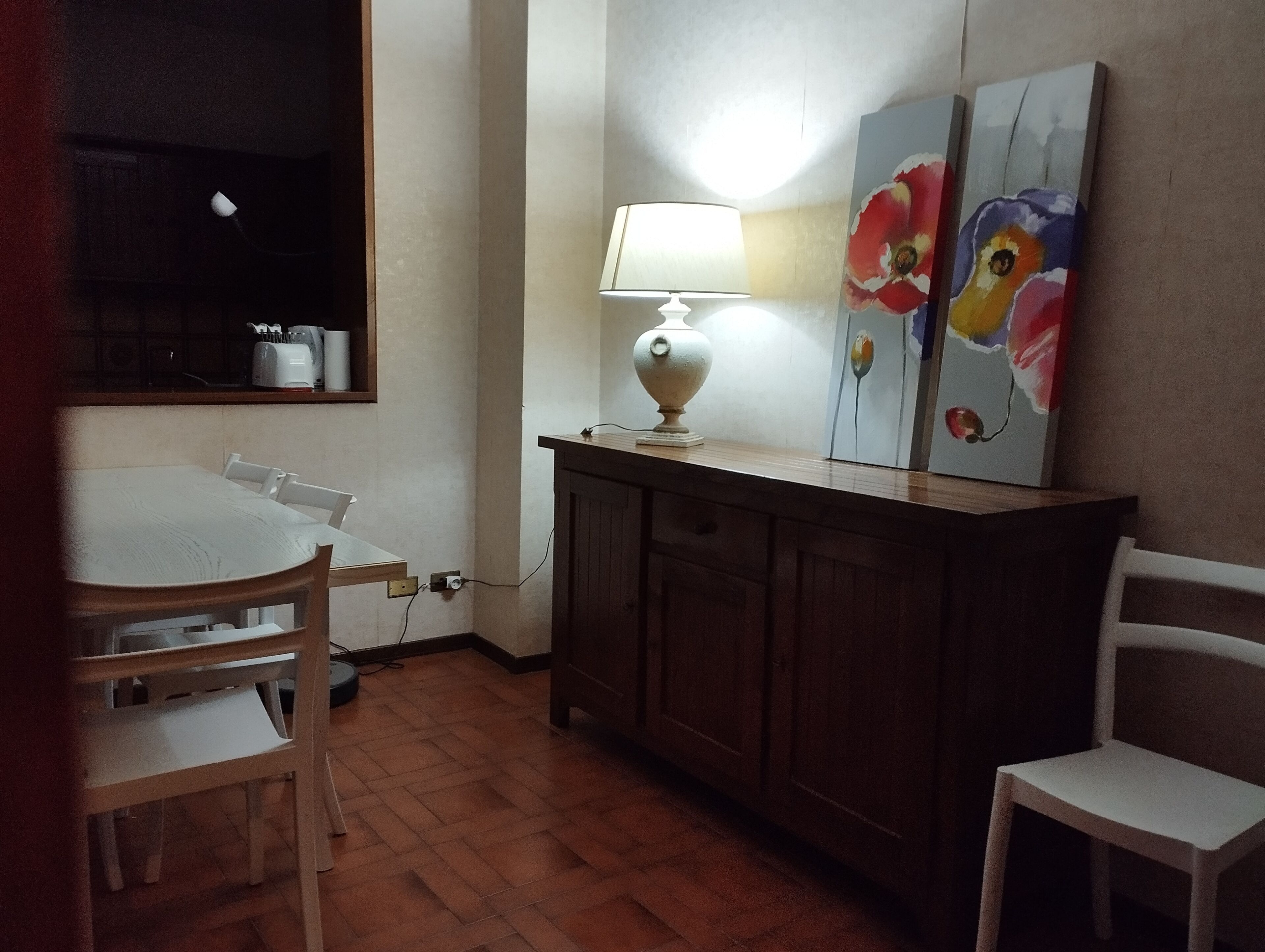 Una zona de menjador amb una taula, cadires, un lampadari i dos quadres a la paret.