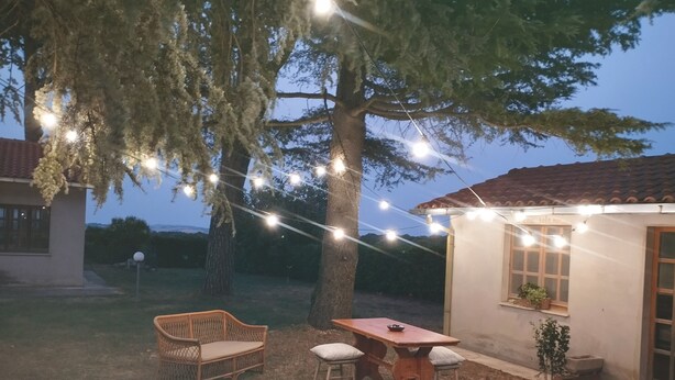 Ein Außenbereich mit Tisch und Stühlen, Lichterketten und einem Baum.