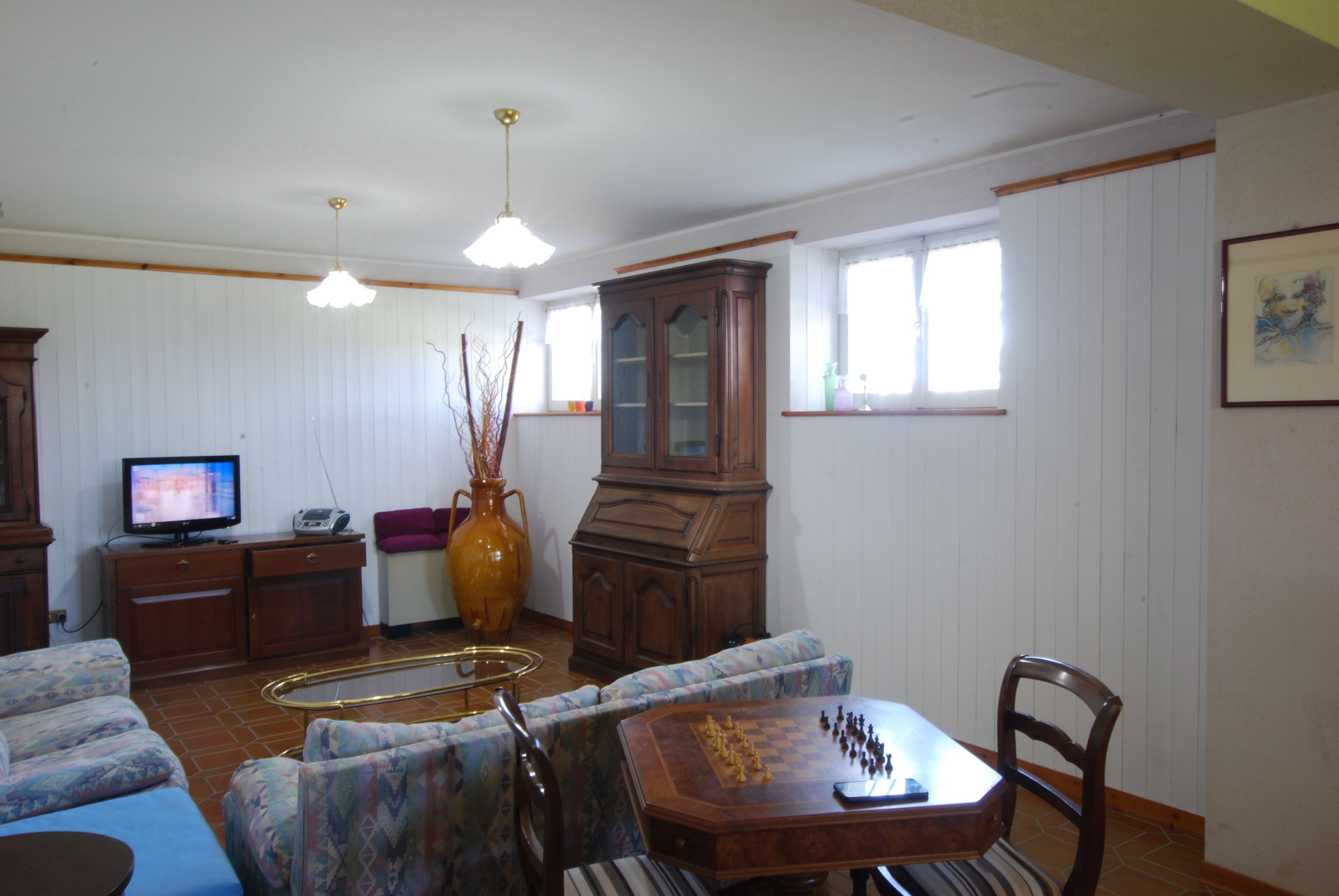 Una sala de estar con un sofá, una mesa de centro de madera con ajedrez, un televisor y un mueble grande.