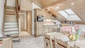 Une cuisine rustique avec des meubles en bois, un sol carrelé, une table à manger avec des chaises et une lucarne.