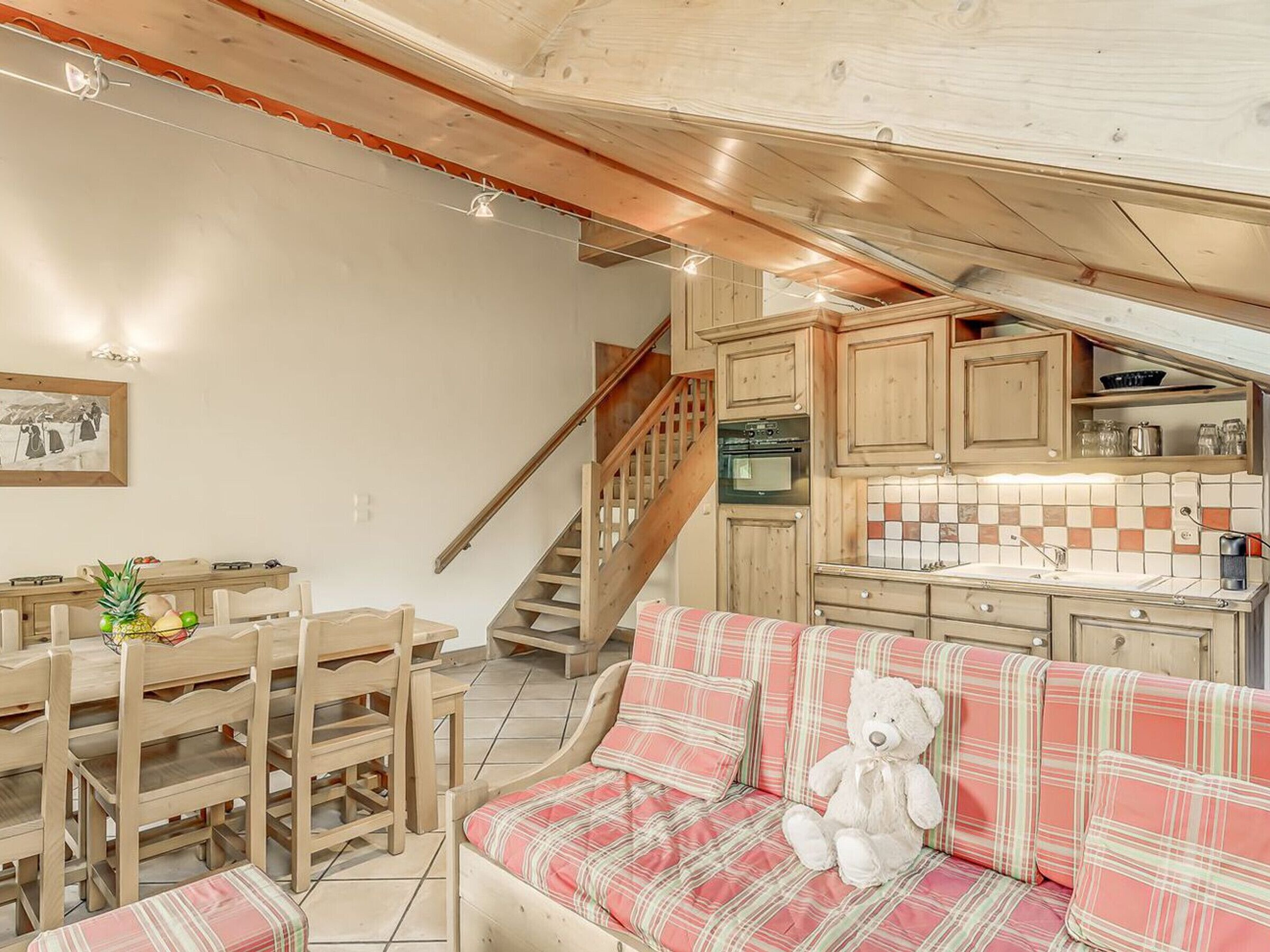 Une cuisine chaleureuse avec des meubles en bois, un coin repas comprenant une table et des chaises, et un escalier menant à l’étage supérieur.