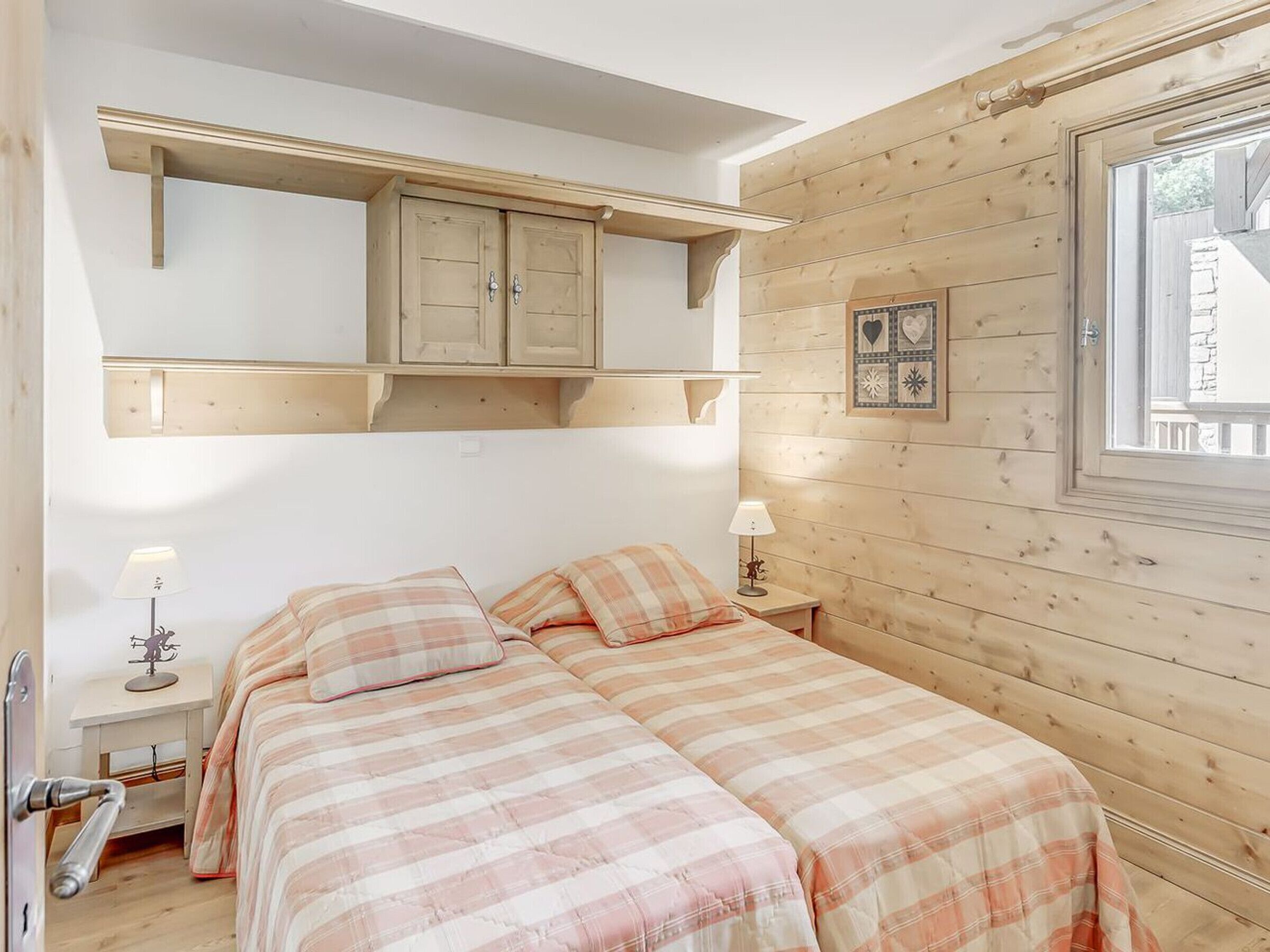 Une chambre avec deux lits, des murs en bois, une fenêtre et une étagère avec des placards.