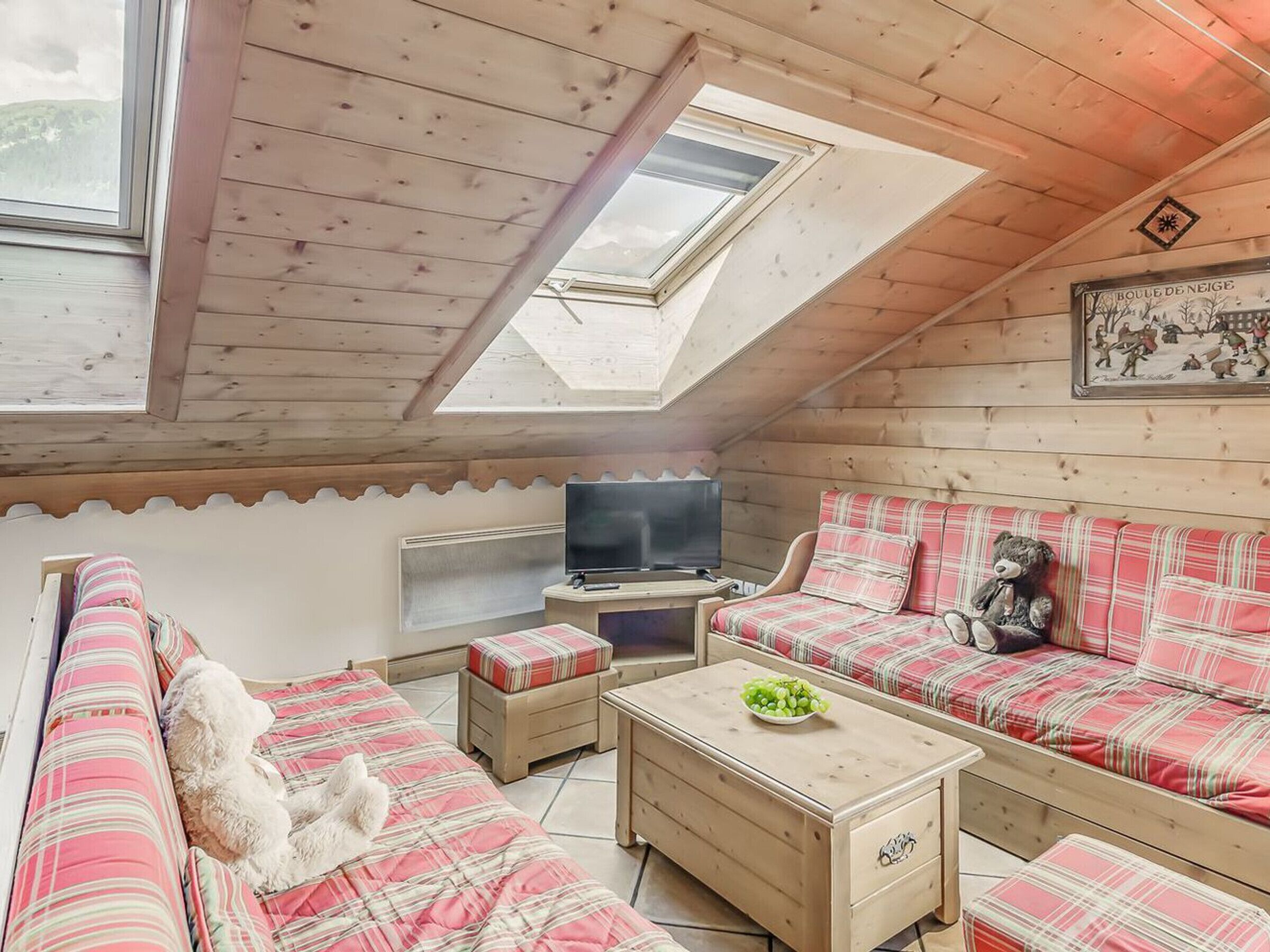 A cozy room with a sloped ceiling, wooden walls, a television, a sofa, a small table, and a window.