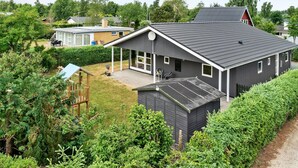 Ein modernes, zweistöckiges Haus mit großem Garten, einer überdachten Terrasse und einem kleinen Geräteschuppen.