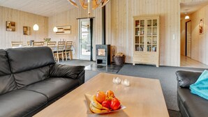 Ein modernes Wohnzimmer mit einem schwarzen Ledersofa, einem Couchtisch mit Früchten, einem Kamin und einer Holzkommode.