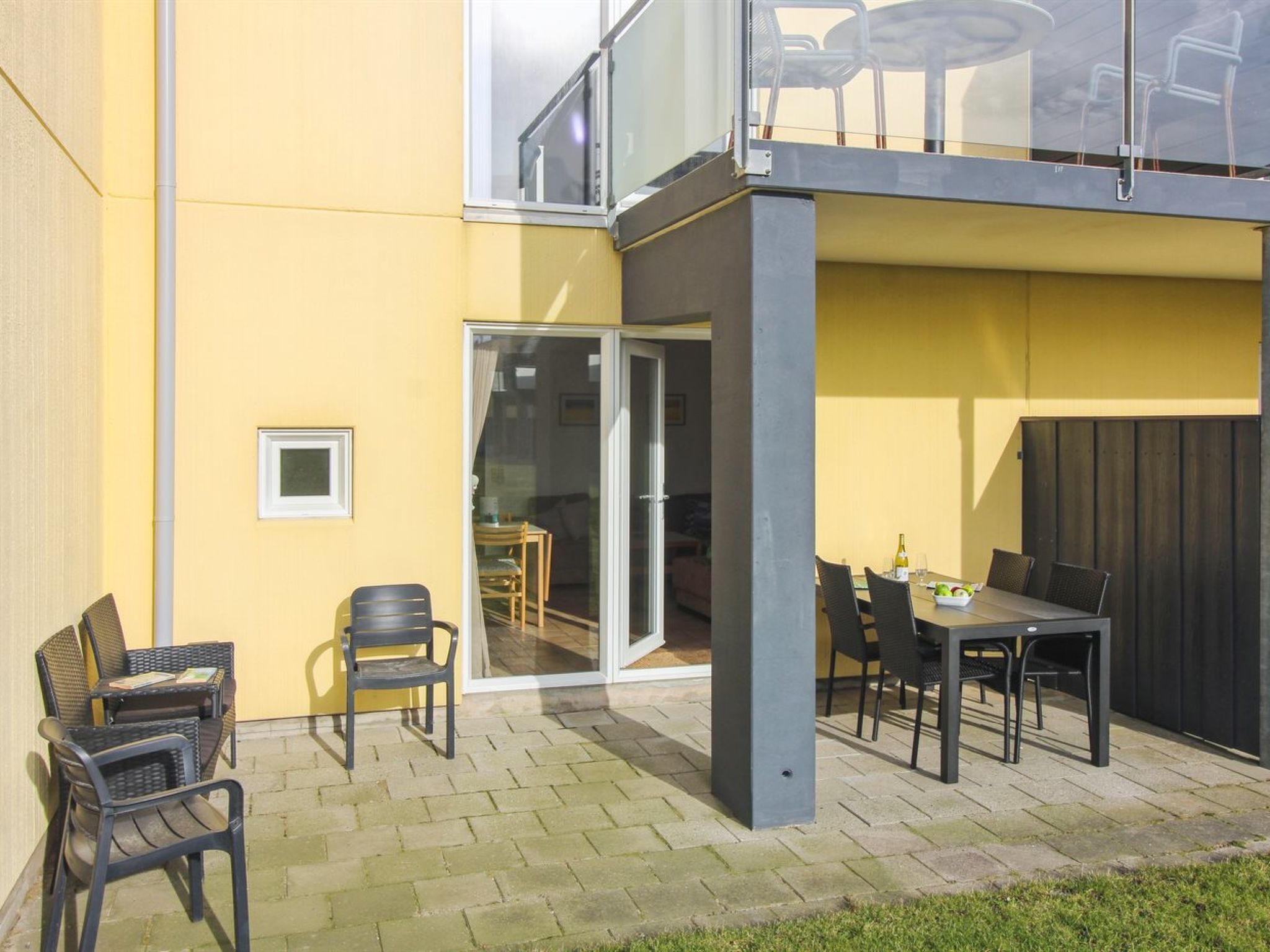 An outdoor patio area with a table and chairs, a sliding glass door leading to an indoor space, and a yellow wall.