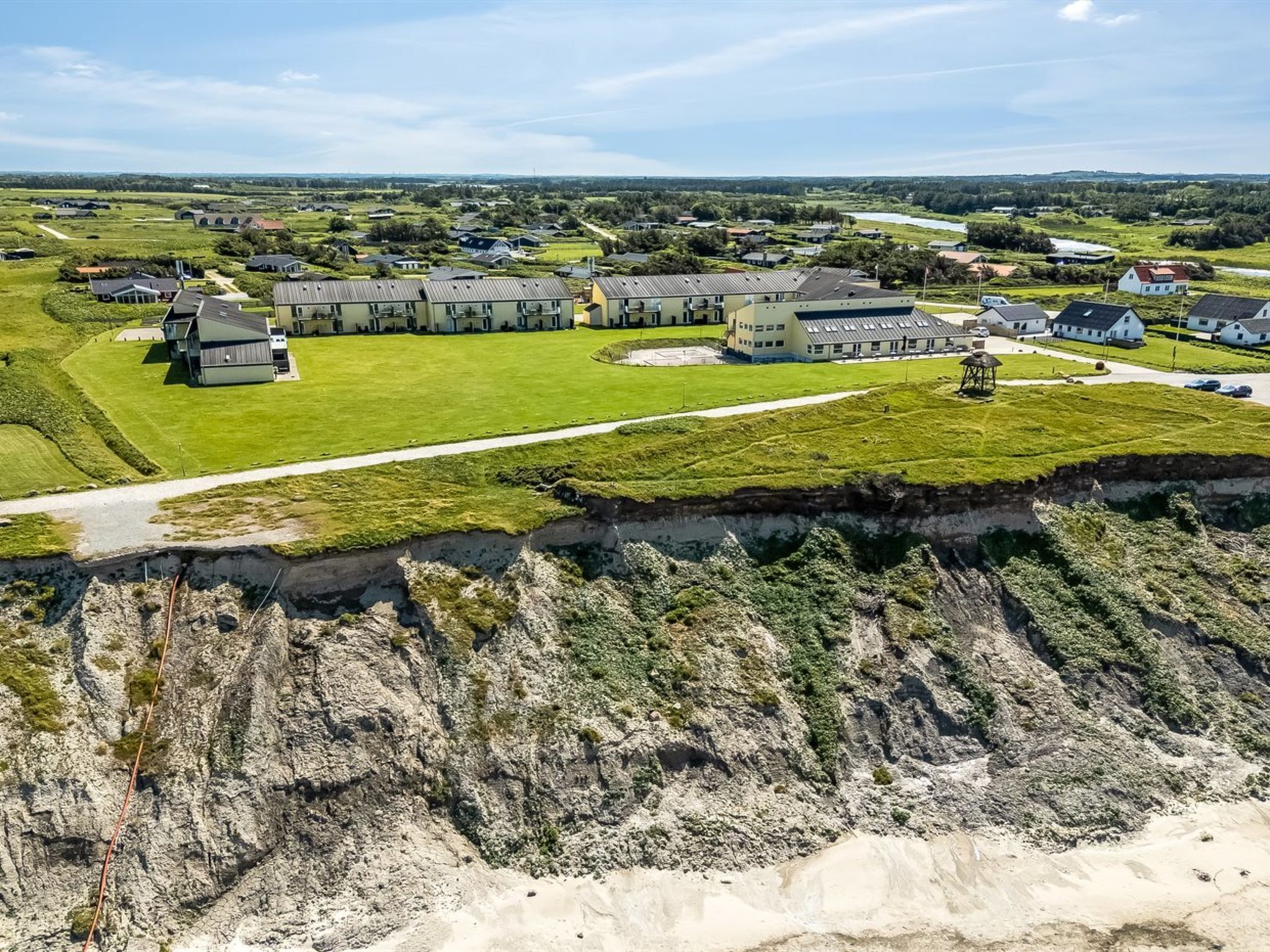 A residential area with houses, a large building with a sloped roof, and a grassy field.