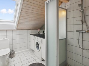 A compact bathroom with a washing machine, toilet, and shower.