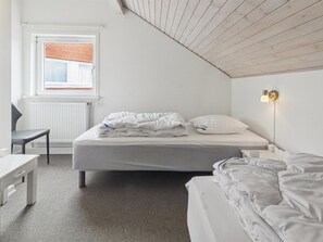 A bedroom with a bed, a desk, a chair, a window with a view, and a wall-mounted lamp.
