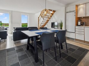 A modern kitchen with white cabinets, a built-in stove, and a dining area with a table and chairs.