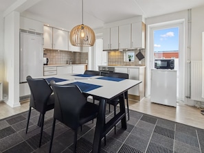 A modern kitchen with white cabinets, a central island, black chairs, and a patterned rug.