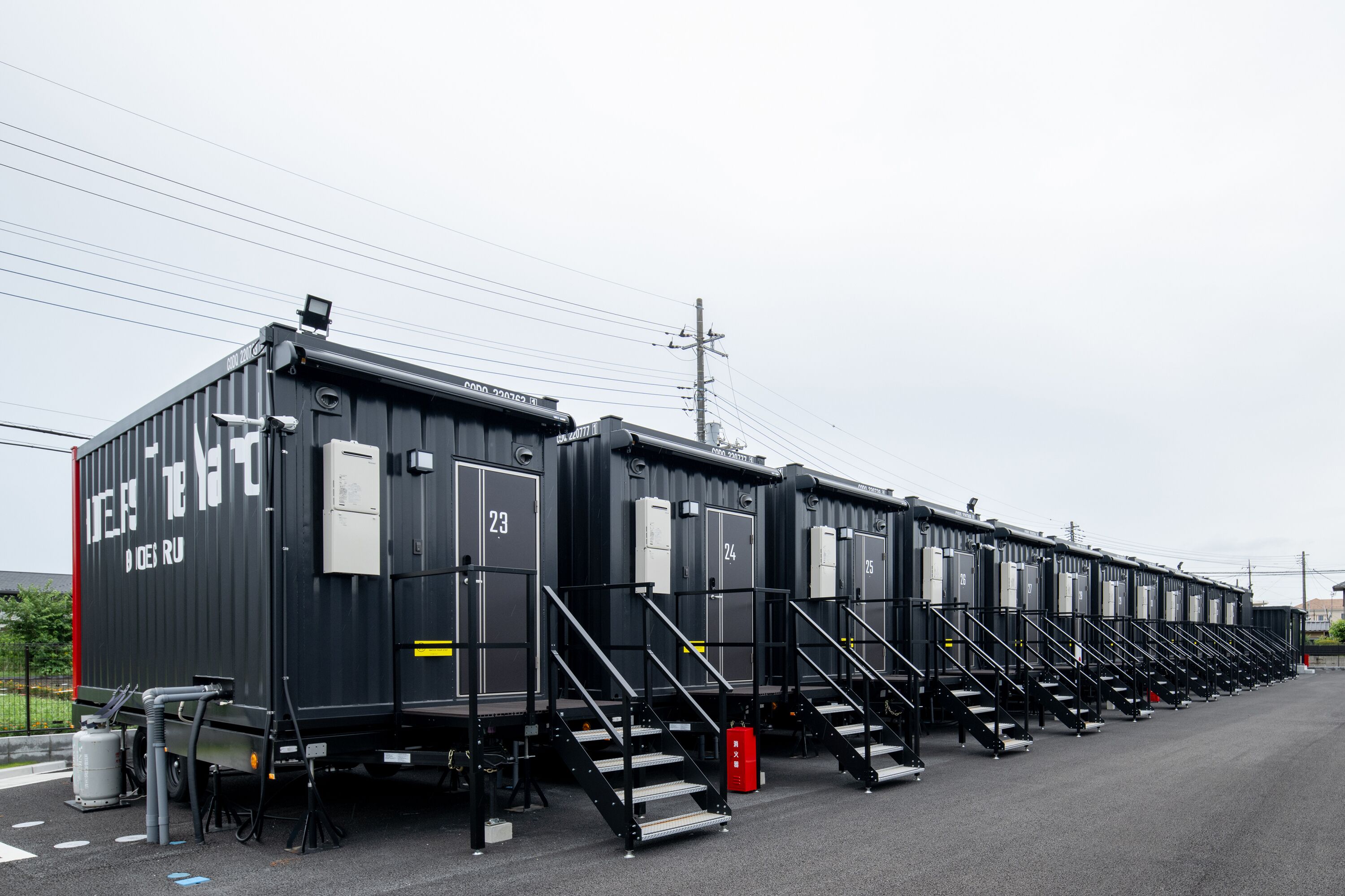 A row of black portable cabins with numbered doors, each with a small staircase leading to the entrance.