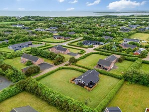 A residential area with houses, green lawns, and a body of water in the background.
