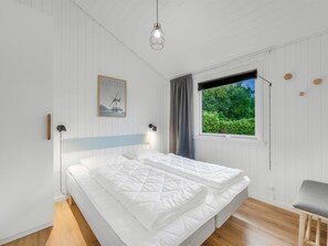 A bedroom with a bed, a window with a view of greenery, a bedside lamp, and a wall-mounted picture.