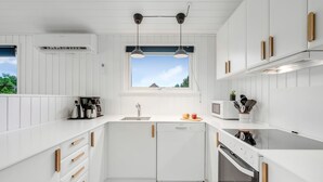 A modern kitchen with white cabinetry, wooden handles, a built-in dishwasher, a microwave, and a stove. - "Picabo" - 750m to the fjord by Interhome (Tarm)