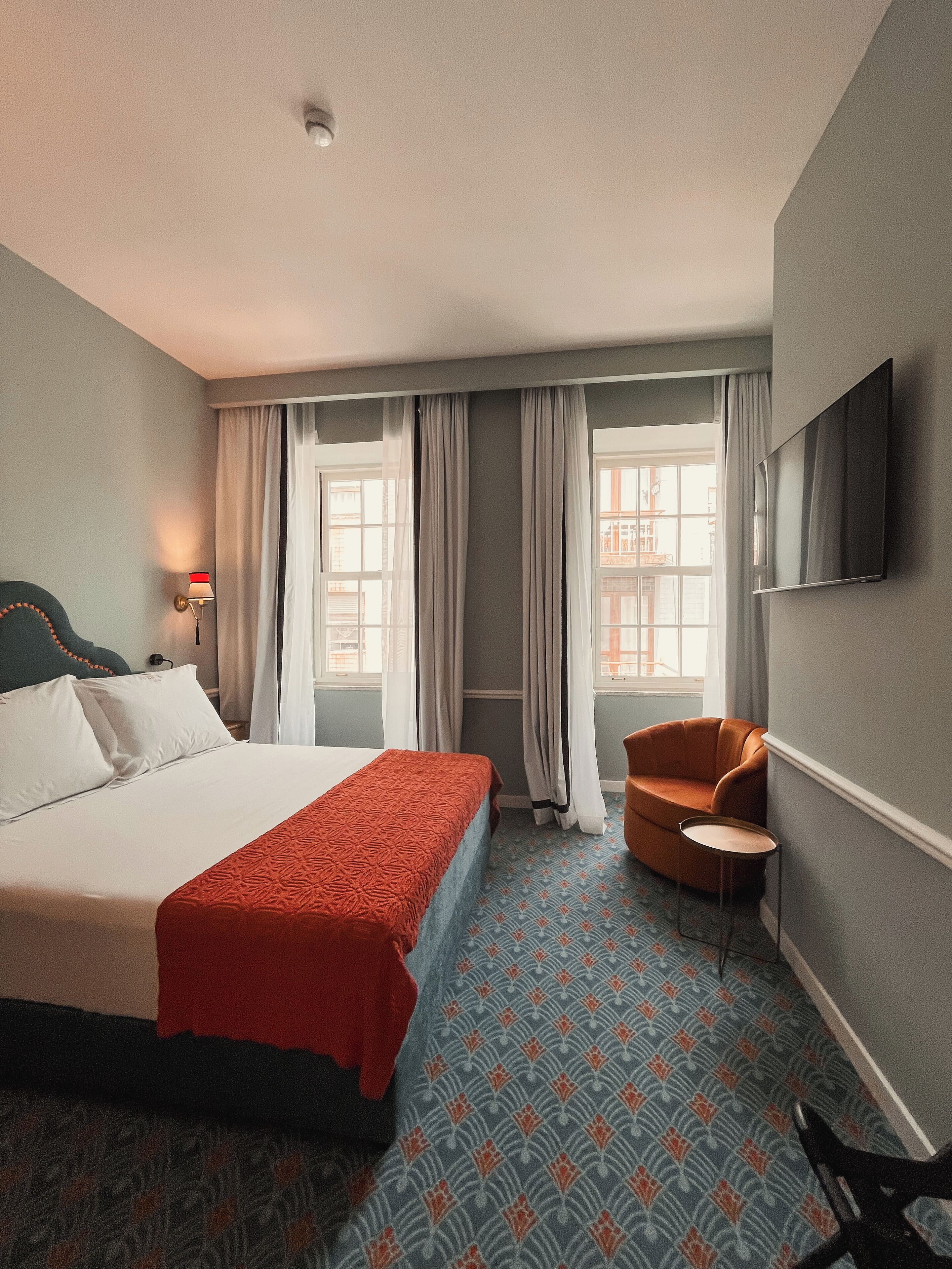Une chambre d’hôtel avec un lit, une chaise, une petite table et un téléviseur fixé au mur.