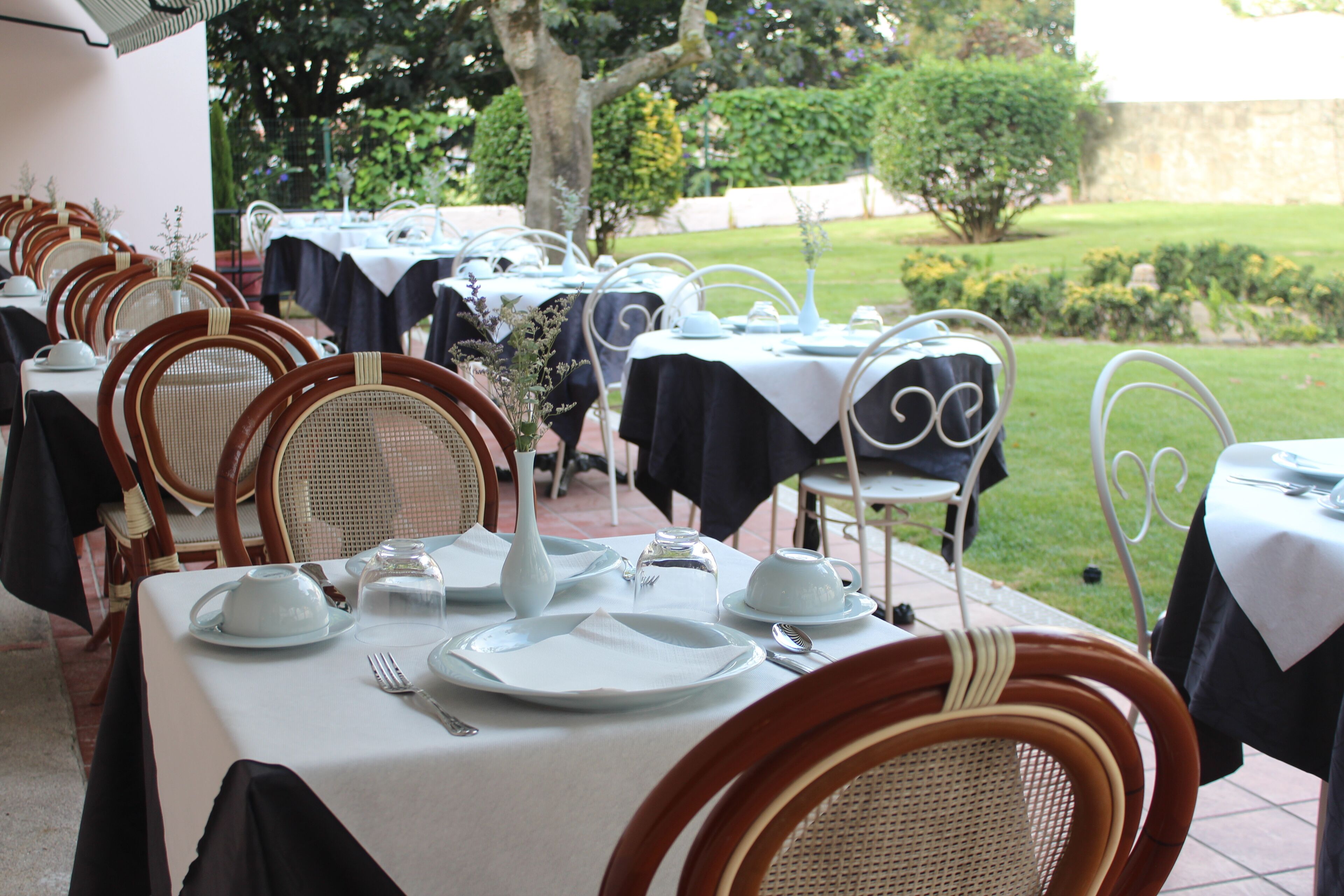 An outdoor dining area with tables set for service, surrounded by greenery.