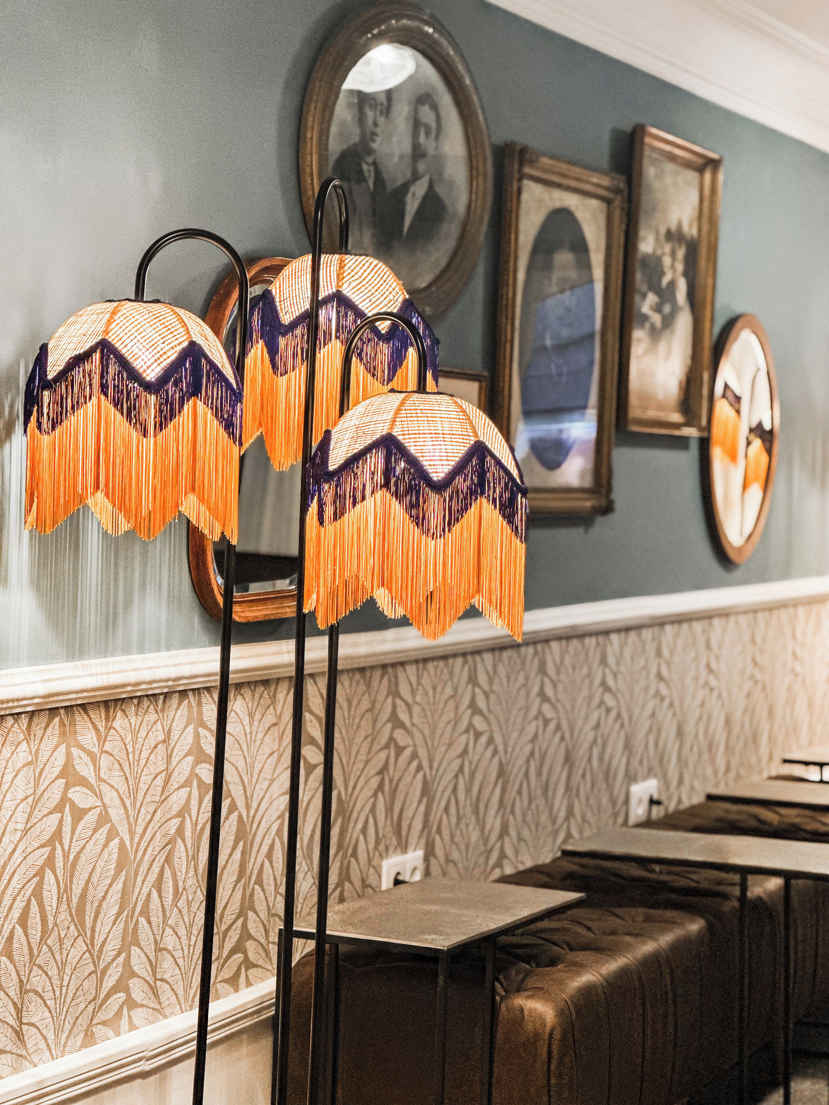 Ein Restaurantinneres mit gemustertem Wandteppich, gerahmten Porträts an der Wand und einem Tisch mit gepolstertem Sitz.