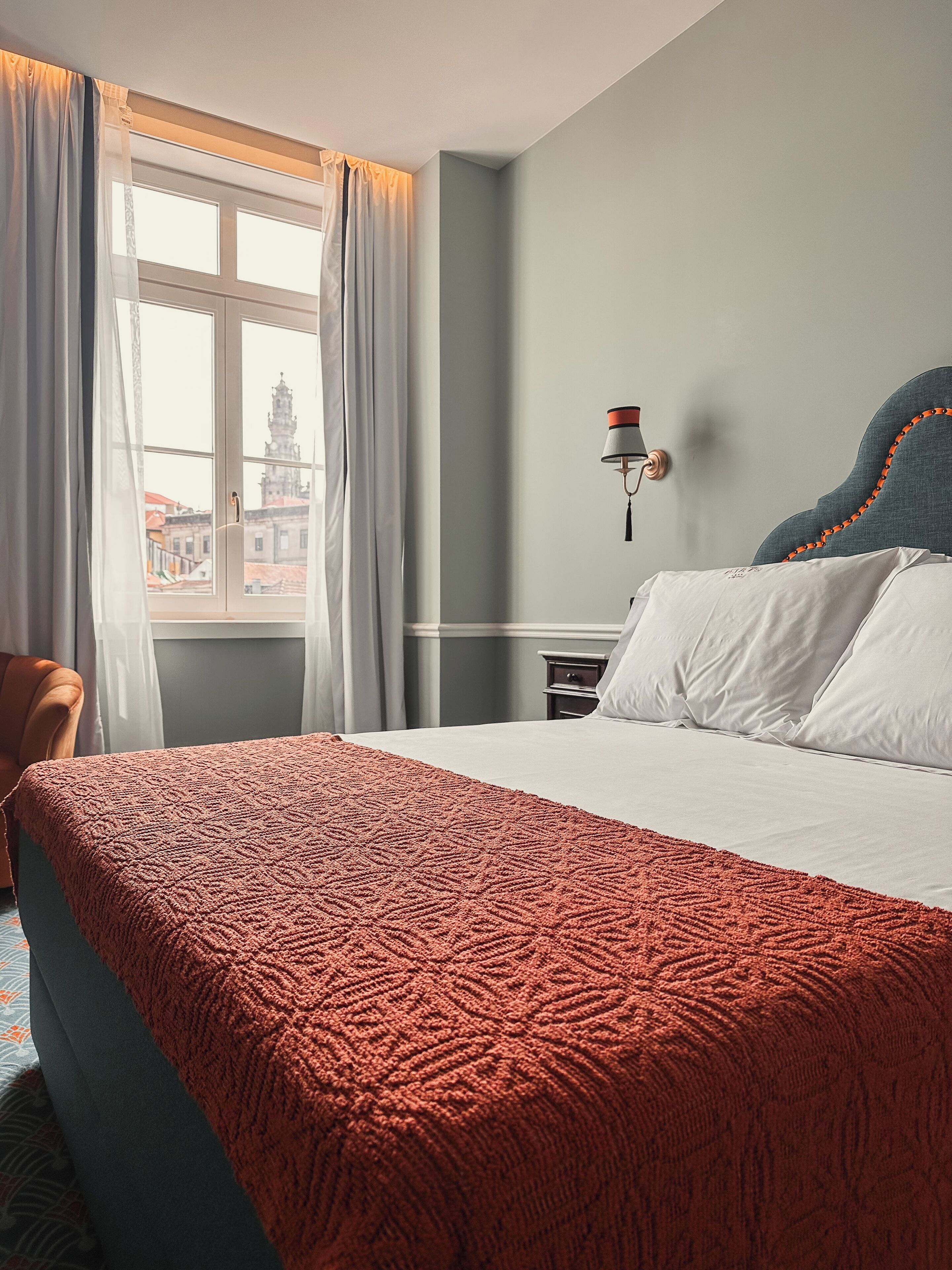 A hotel room with a large bed, a nightstand, a lamp, and a window with curtains.
