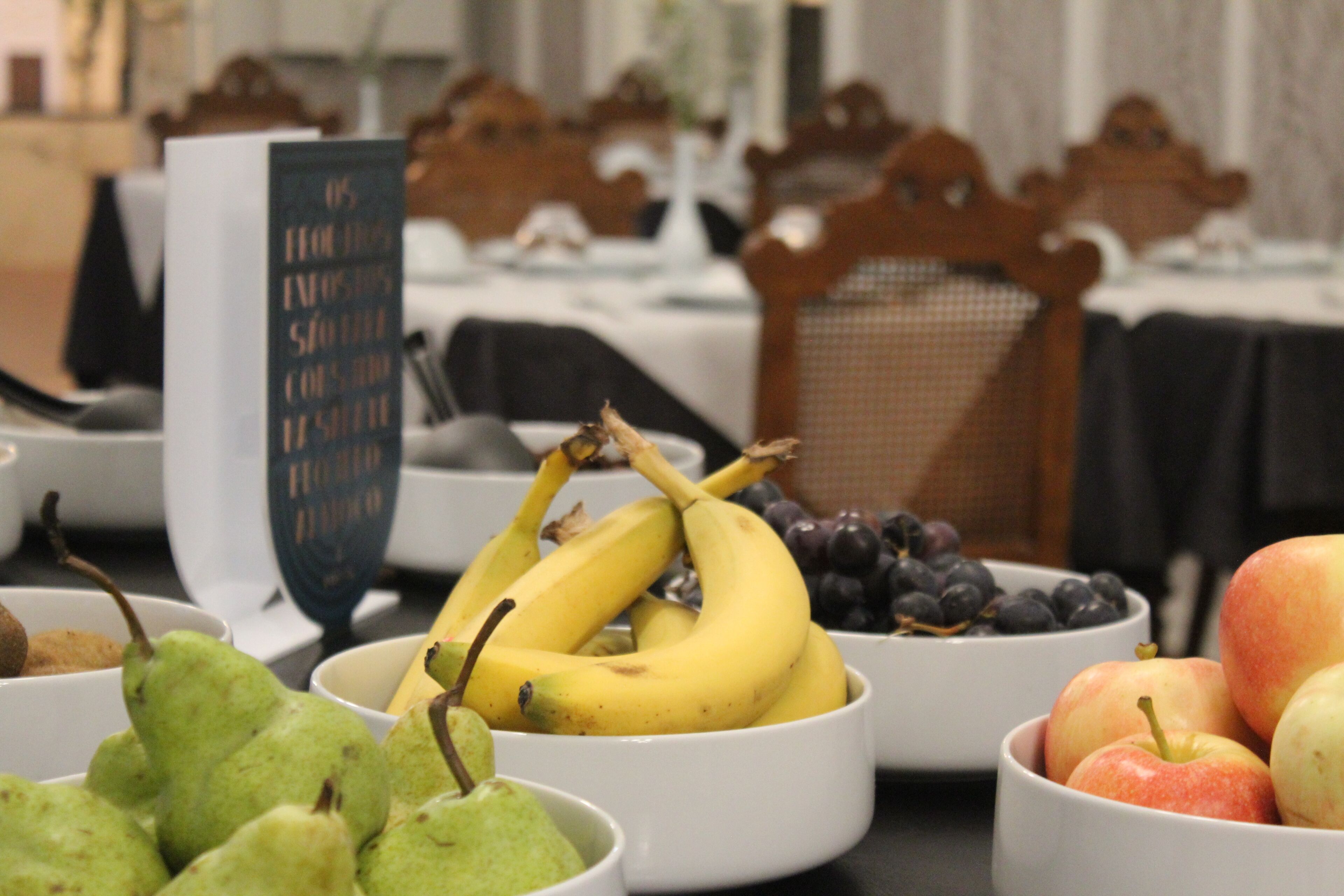 A table with bowls of fruit including bananas, grapes, pears, and apples.