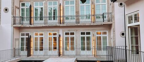 Un edificio de varios pisos con balcones, un arco de piedra y un césped bien cuidado.