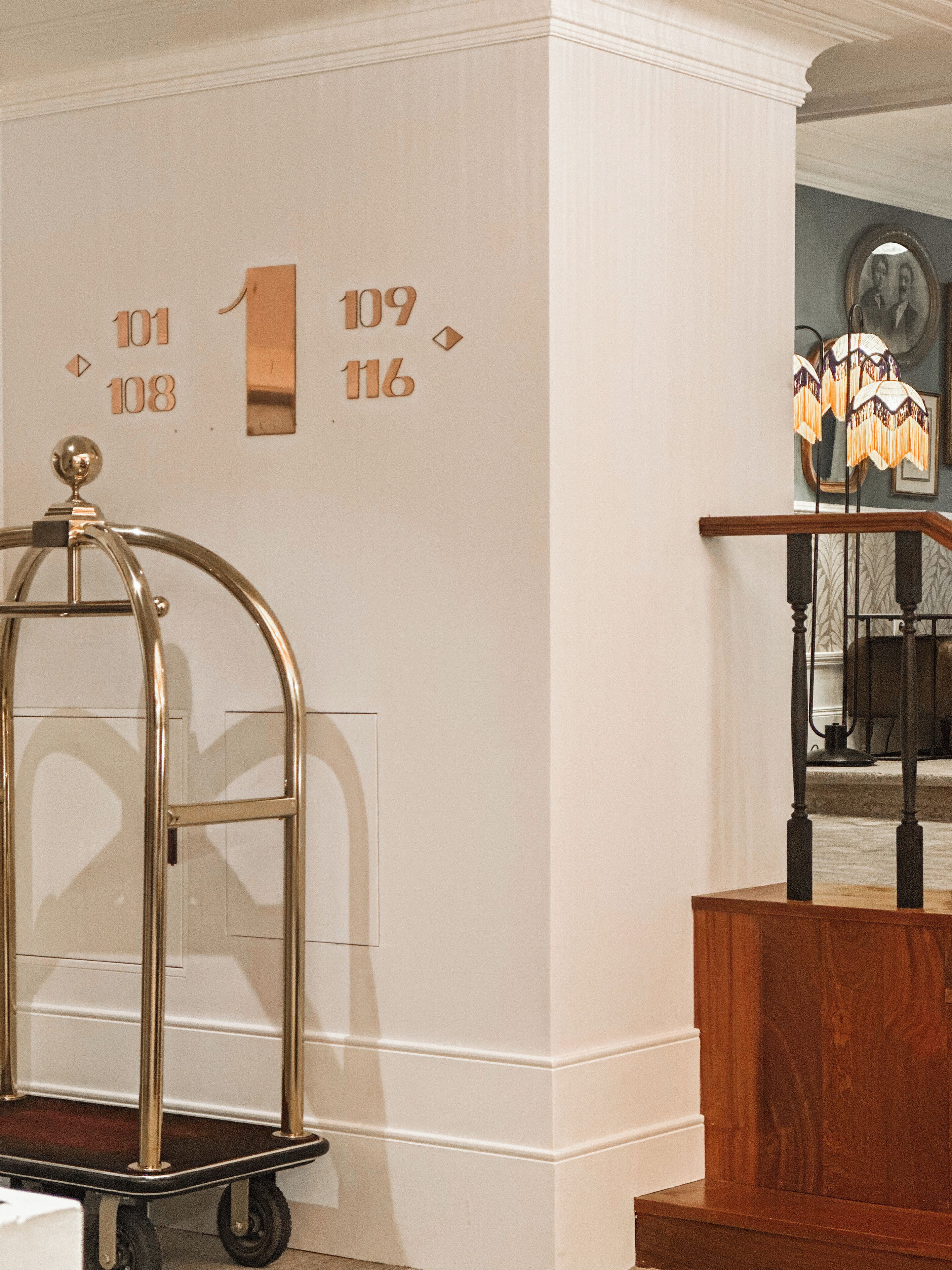 A hotel interior with a wall-mounted number sign, a wooden reception desk, and a chandelier.