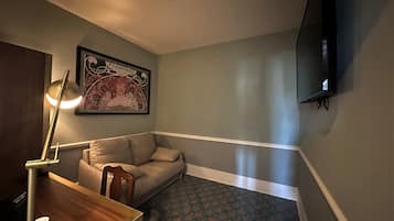 Una habitación con un sofá, una mesa con tazas, un cuadro en la pared y un televisor de pantalla plana montado en la pared.