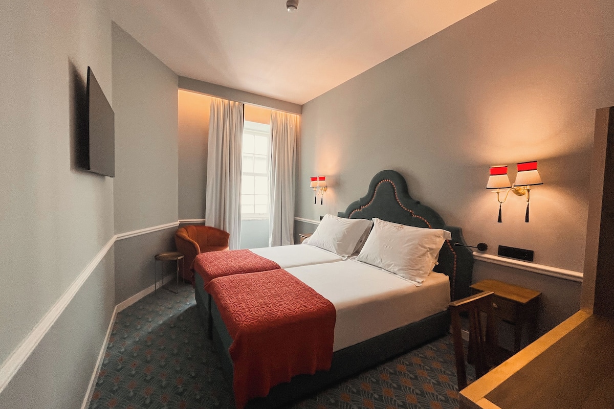 A hotel room with a double bed, a chair, a desk, and a window with curtains.