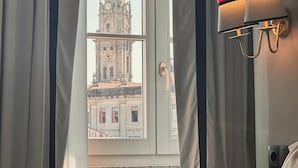 A room with a view of a historic tower through a window, curtains, and a wall-mounted lamp. - GRANDE HOTEL PARIS by STAY HOTELS (Porto)